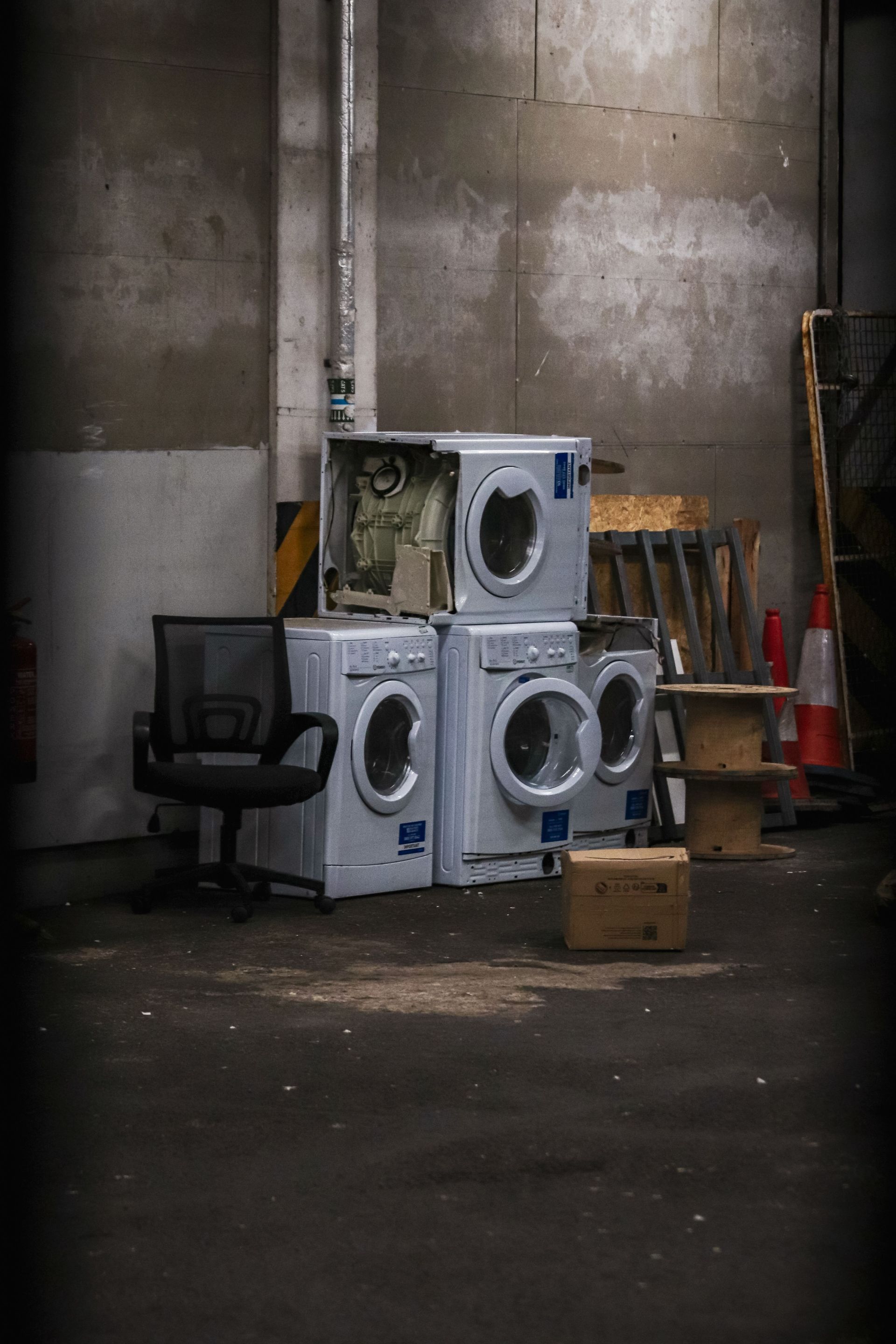 An urban alley corner with discarded washing machines and office chair, showing decay.